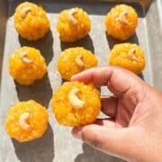 A hand holding boondi laddu and the remaining laddus on a sheet tray.
