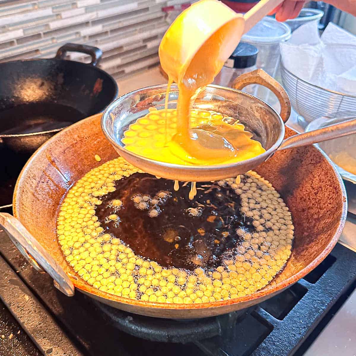Laddu batter being poured into a laddu laddle and fried into little boondis.